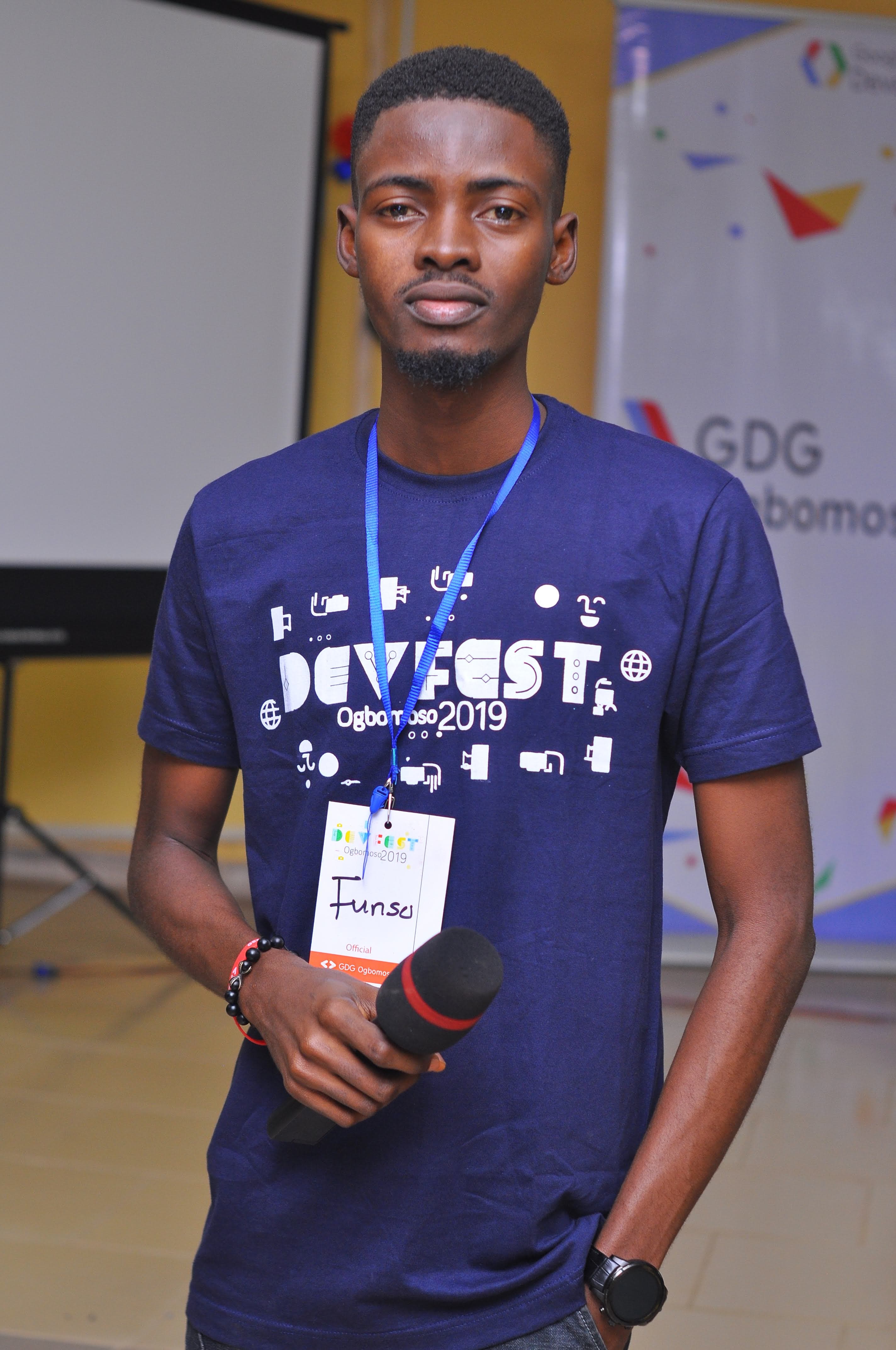 An attendee holding a microphone beside a GDG banner at DevFest Ogbomoso 2019