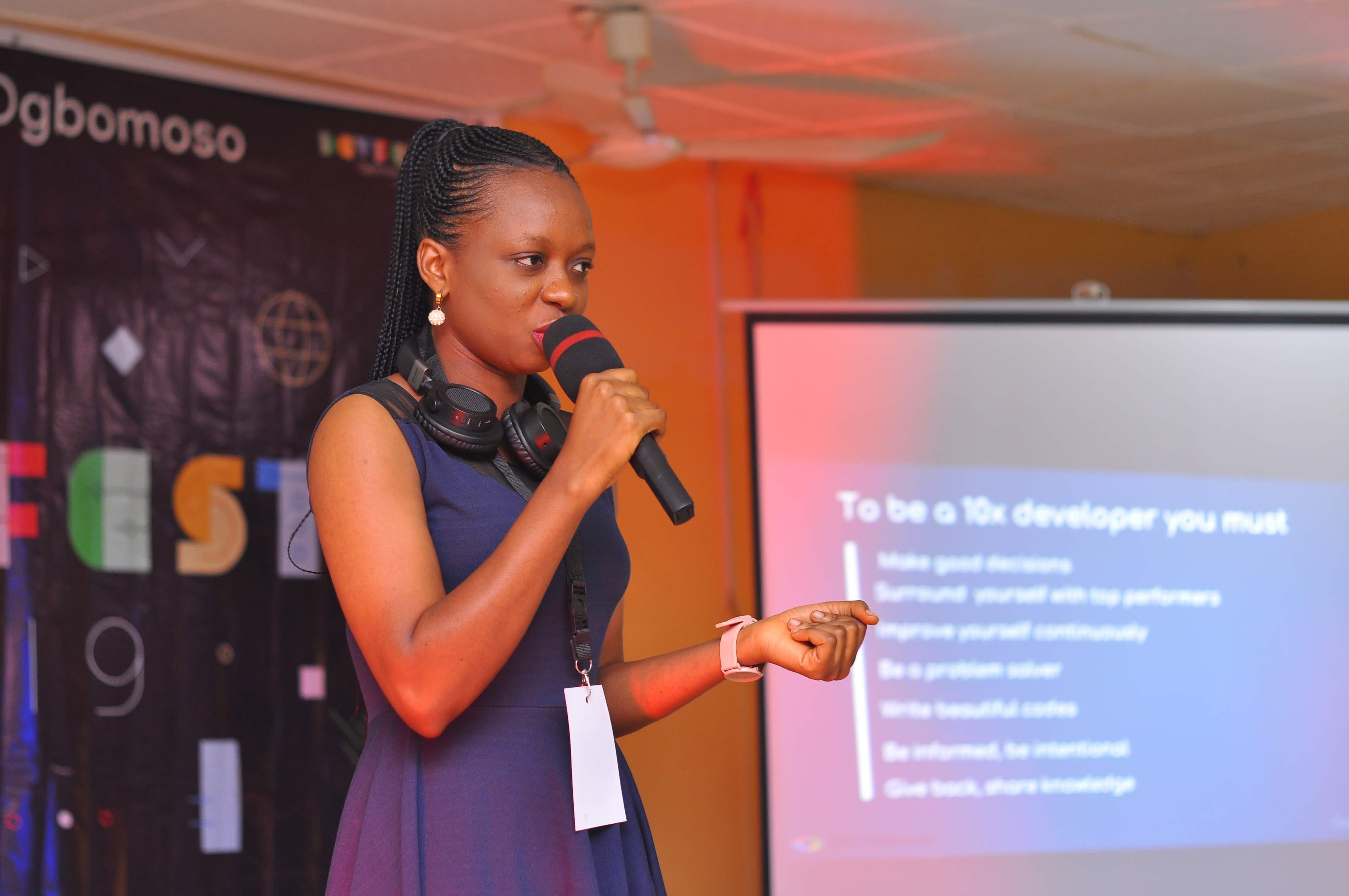 A speaker presenting beside a projected slide at DevFest Ogbomoso 2019