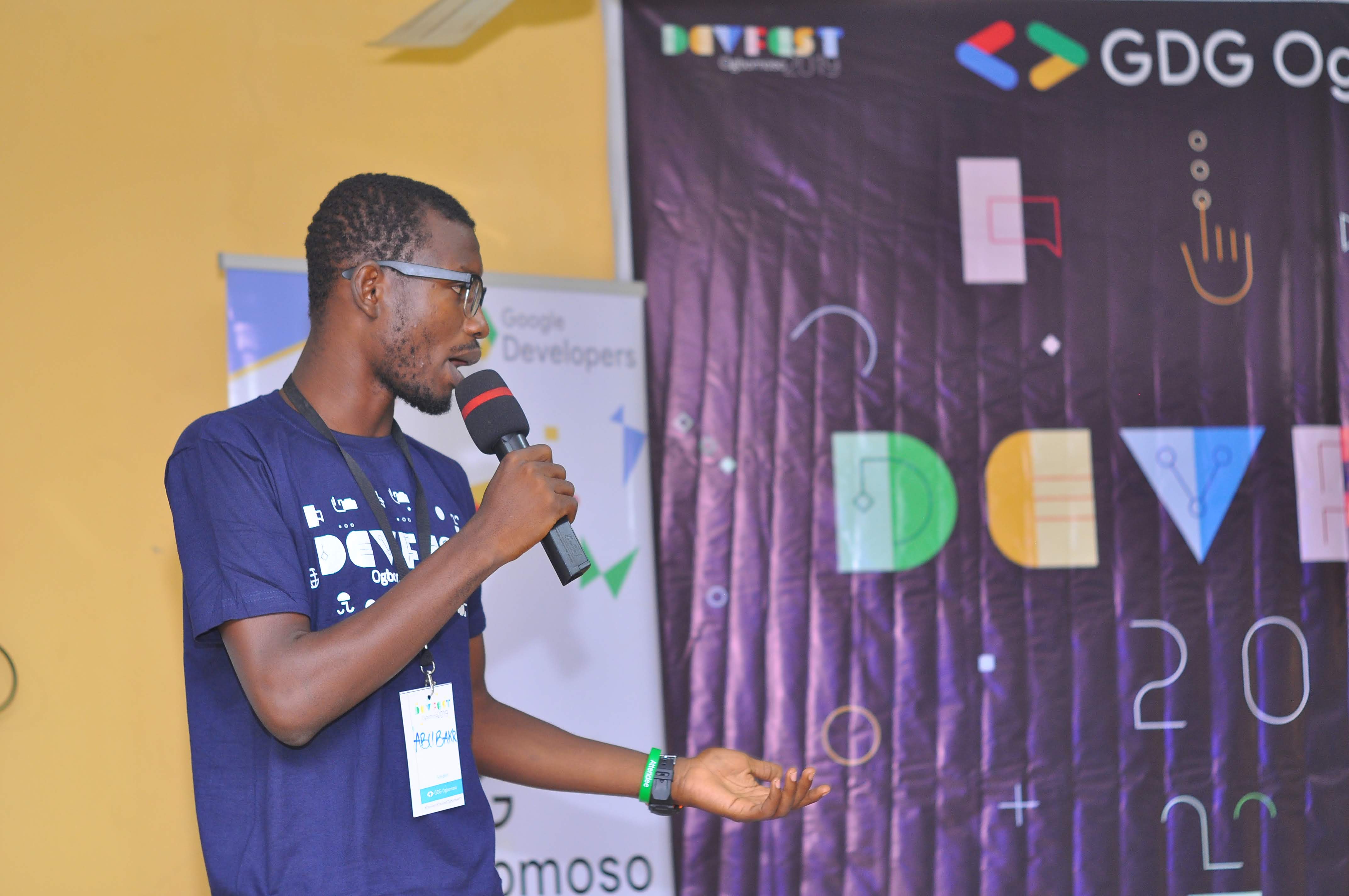 A speaker with a microphone by the DevFest backdrop at DevFest Ogbomoso 2019