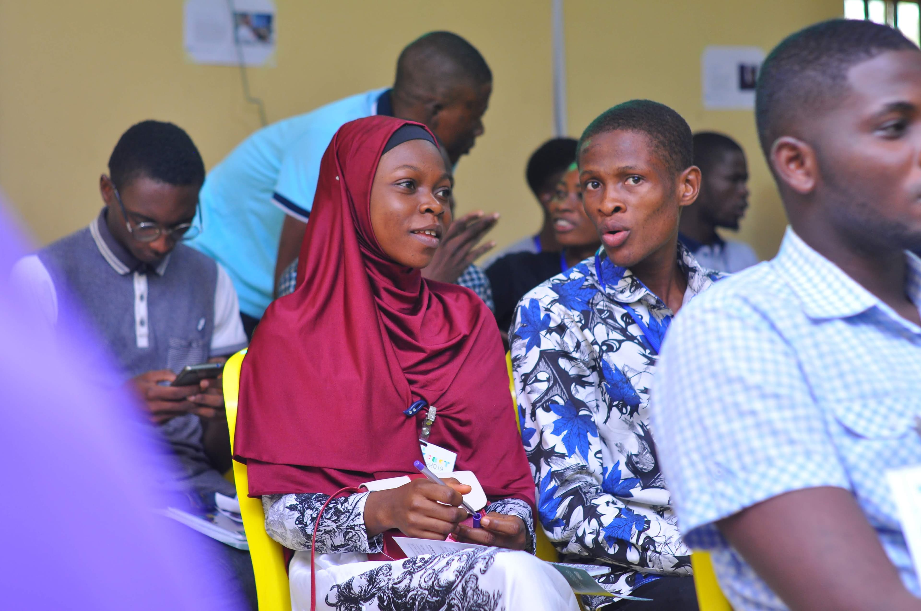 Seated attendees, one holding a pen and paper at DevFest Ogbomoso 2019
