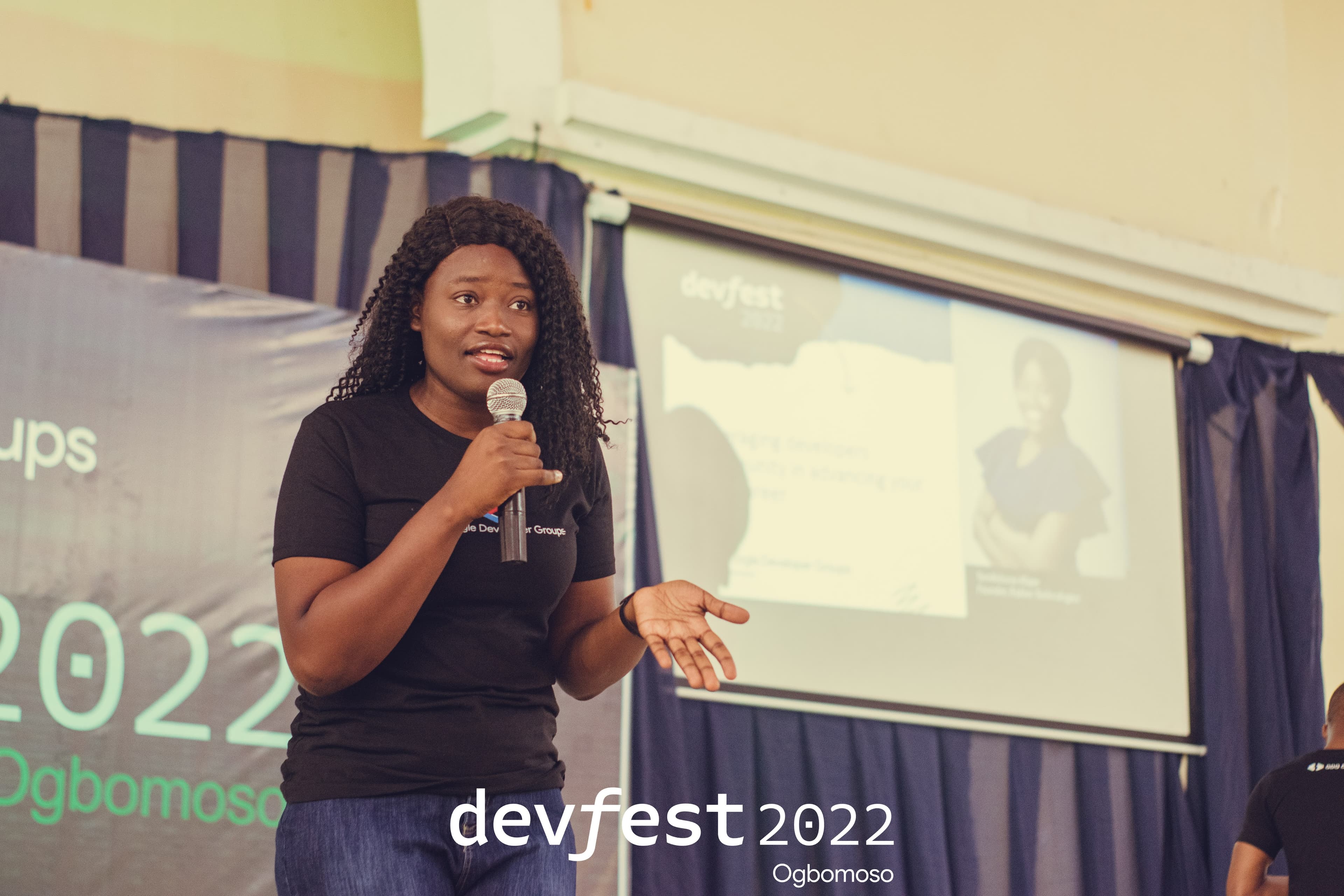 A speaker holding a microphone beside the screen at DevFest Ogbomoso 2022