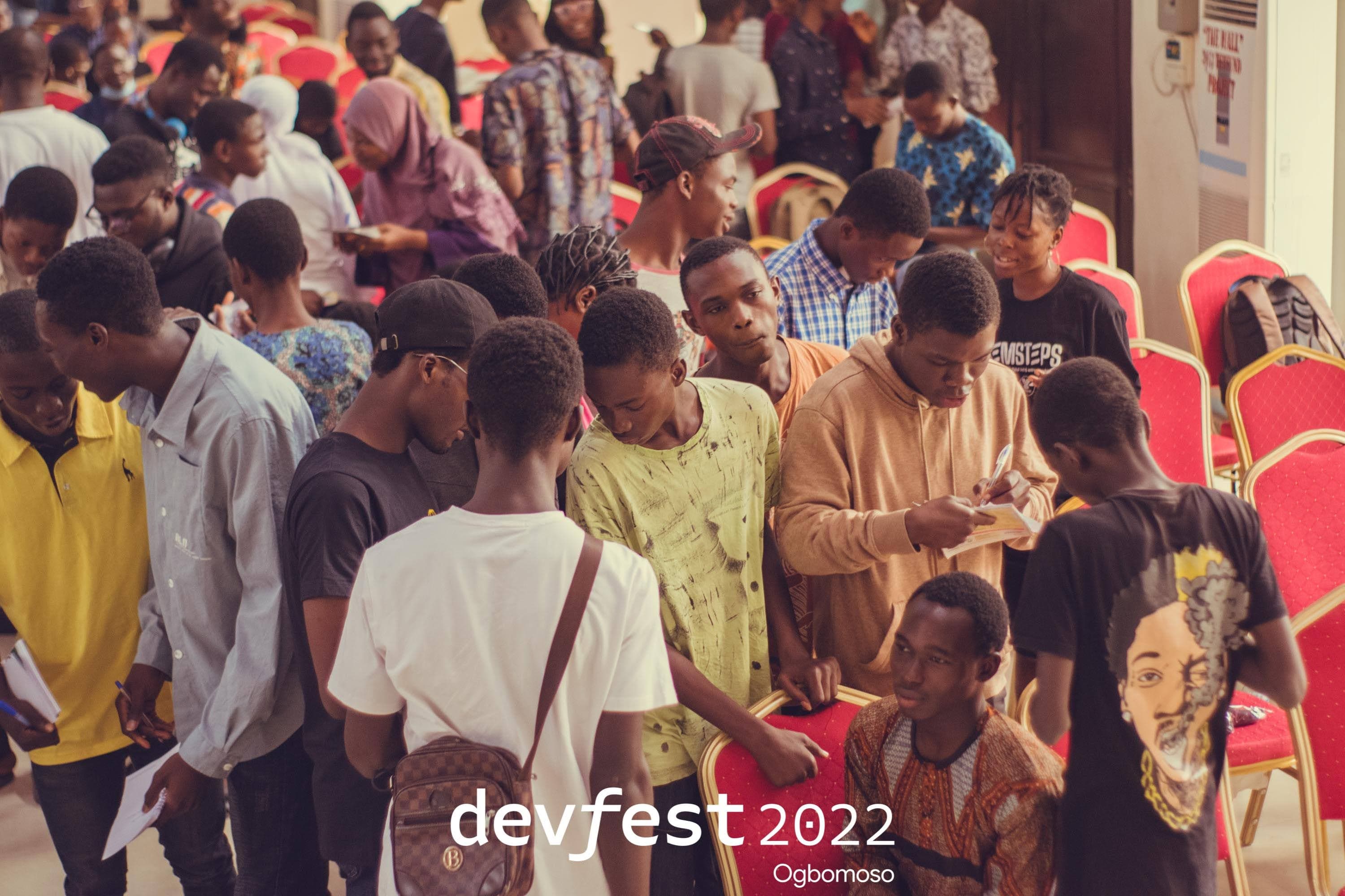Attendees gathered among the chairs, one writing on paper at DevFest Ogbomoso 2022