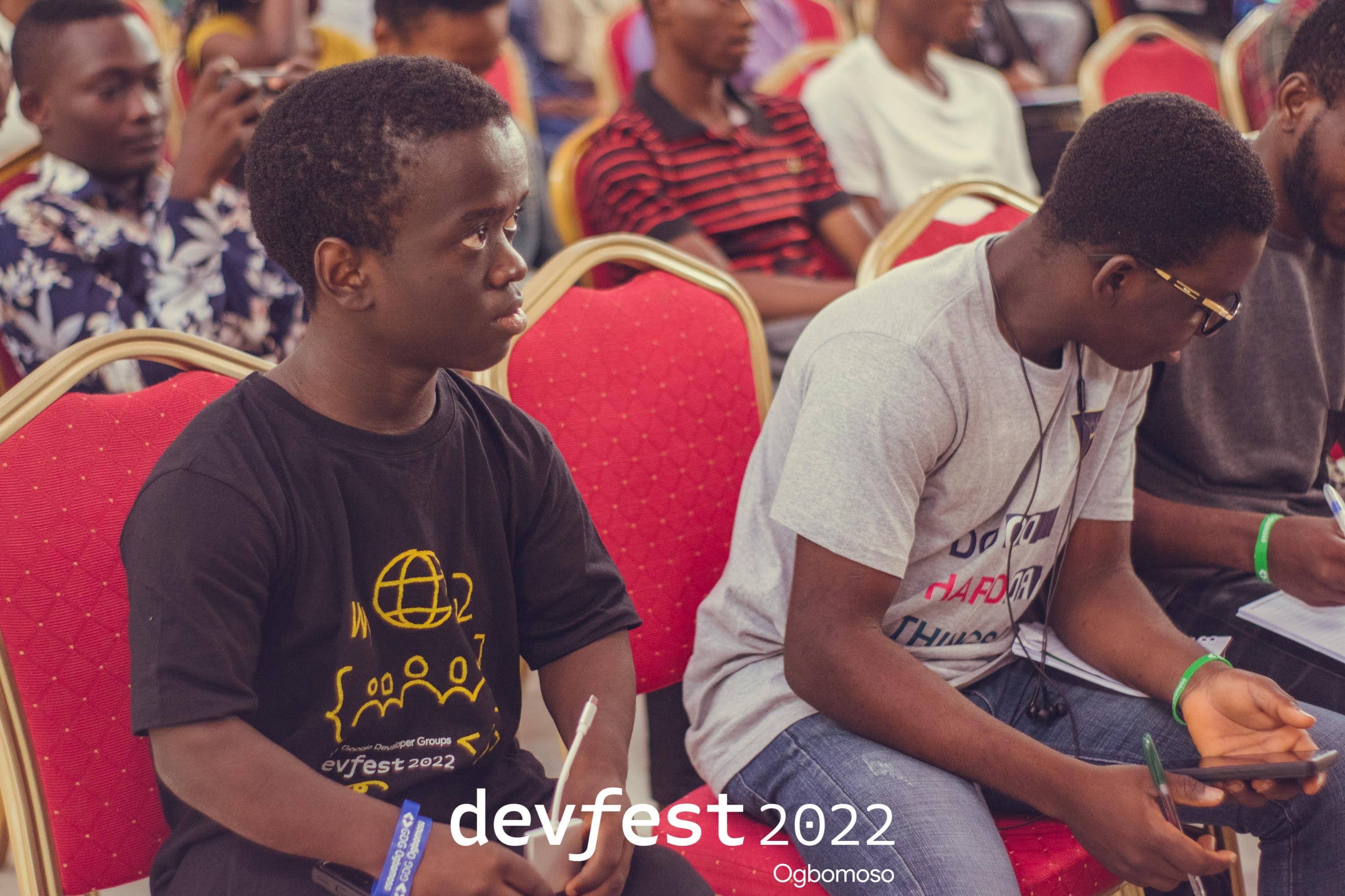 Seated attendees, one looking down at a phone at DevFest Ogbomoso 2022