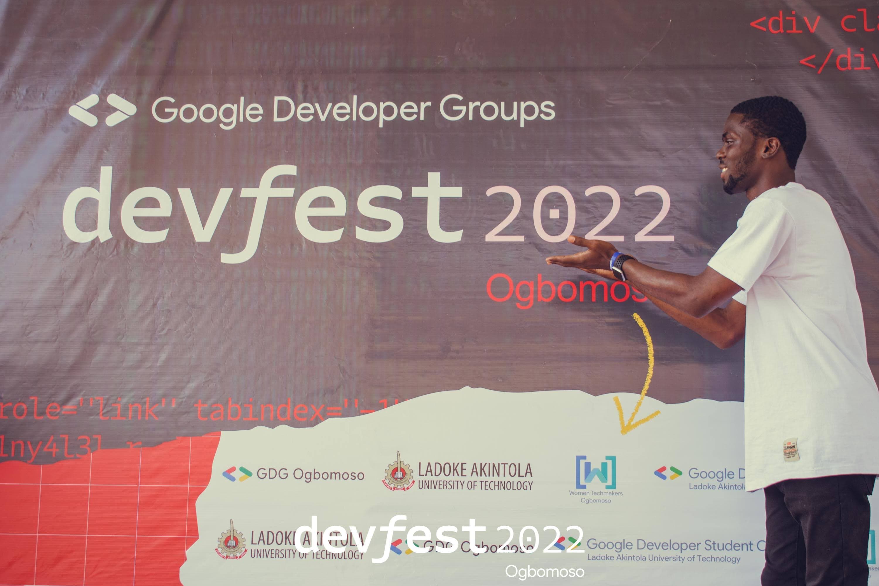 An attendee gesturing toward the DevFest backdrop at DevFest Ogbomoso 2022