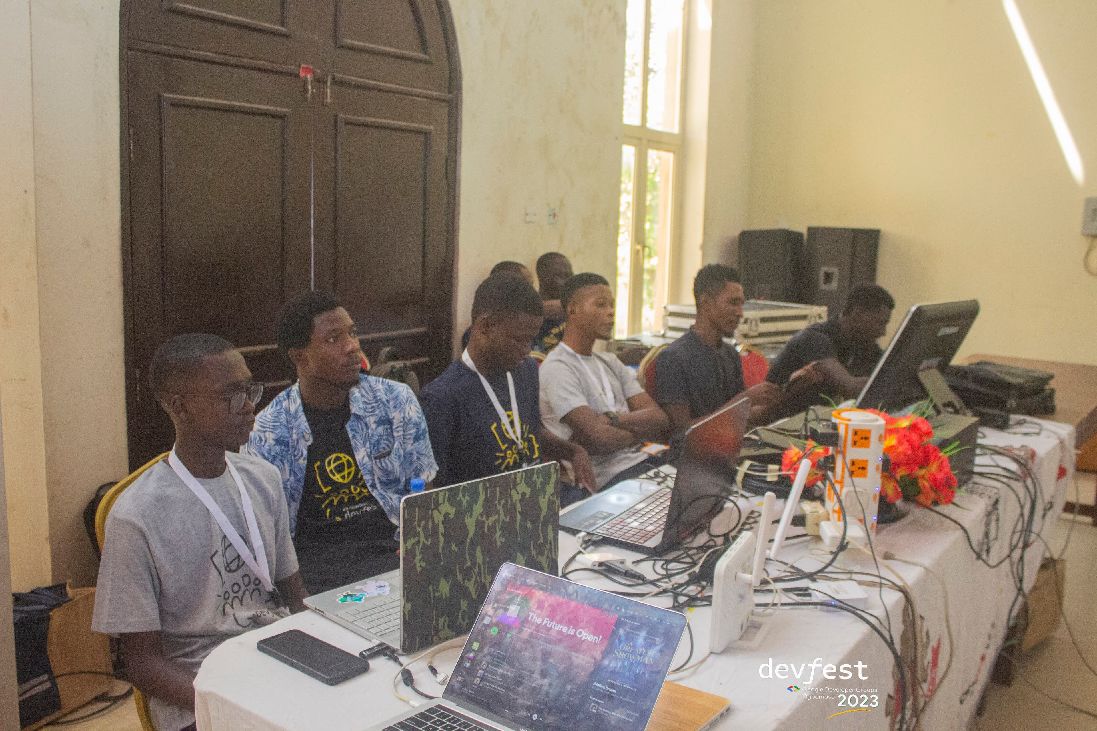Attendees seated at a table of laptops and cables at DevFest Ogbomoso 2023