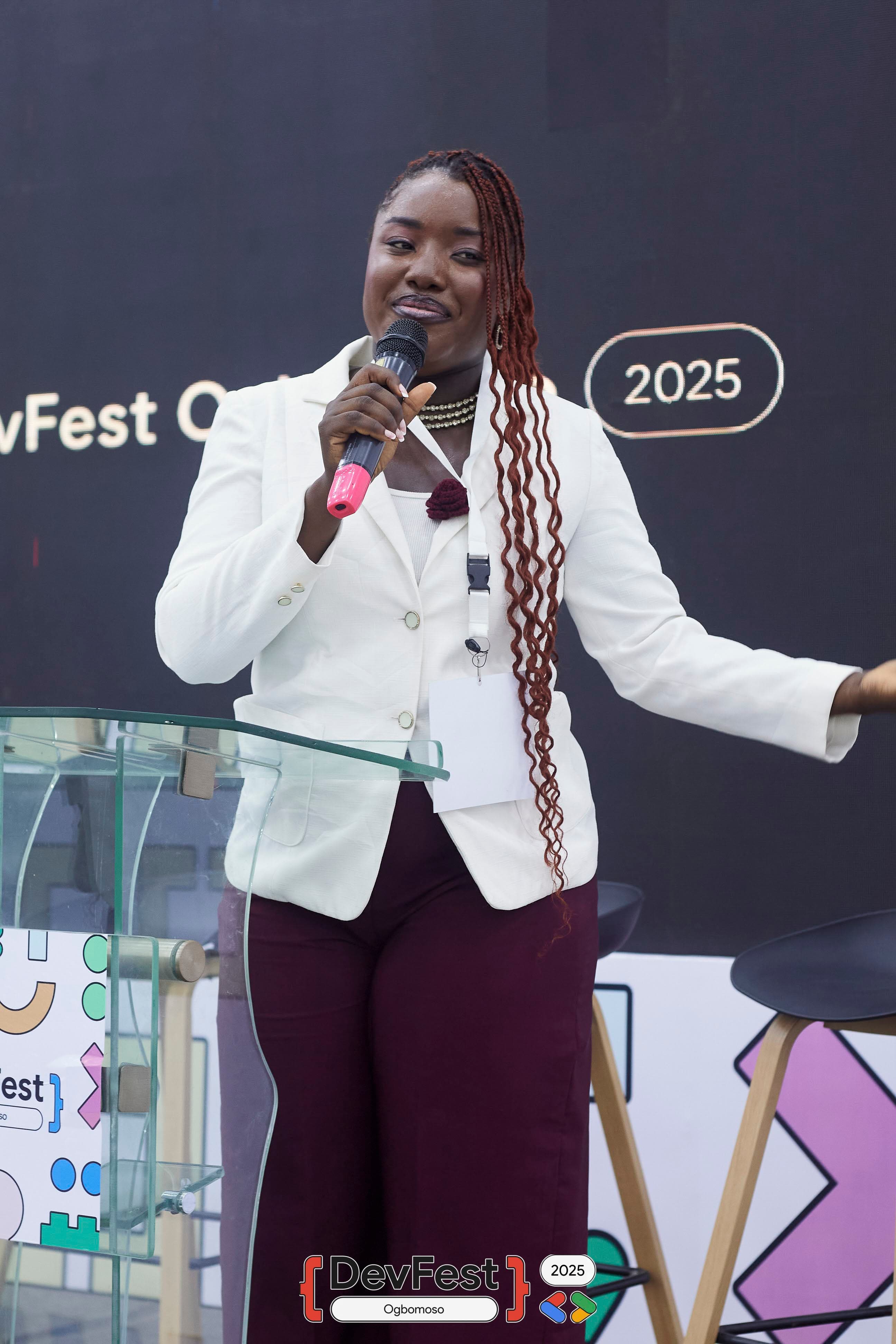 A speaker with a microphone beside a glass lectern at DevFest Ogbomoso 2025