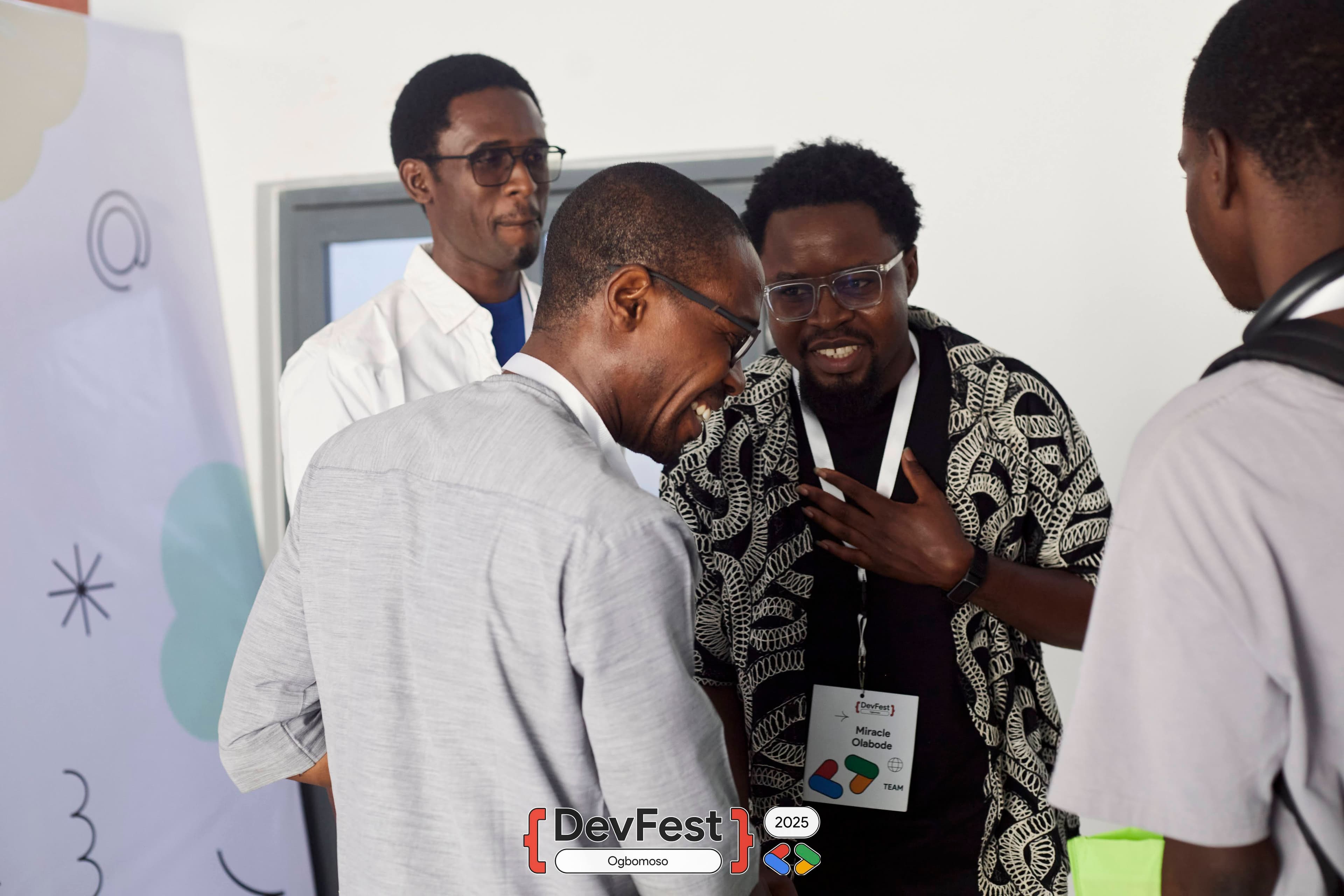 Four people chatting and smiling beside a decorated banner at DevFest Ogbomoso 2025