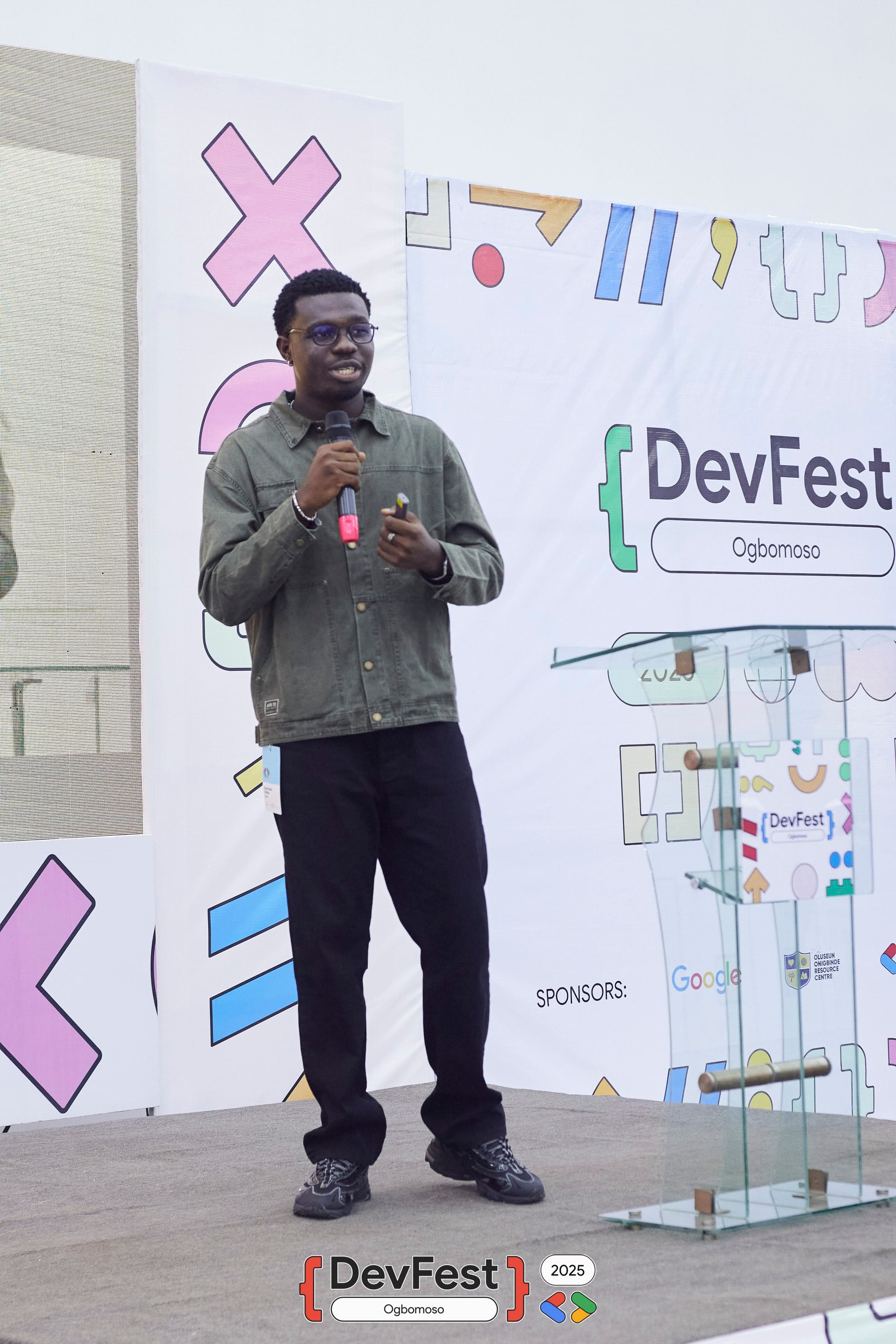 A speaker with a microphone on the DevFest stage at DevFest Ogbomoso 2025